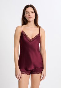 Camisola in raso bordeaux con rifiniture in pizzo e spalline regolabili, abbinata a pantaloni corti coordinati con dettagli in pizzo all'orlo.