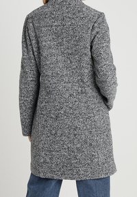Šedý kabát z vlněné směsi s texturovaným povrchem, dlouhými rukávy a límcem, sahající po polovinu stehen, s jednoduchým, nenápadným designem.