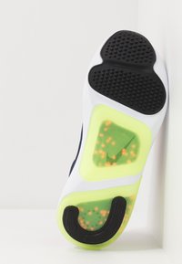 Sportovní obuv s černou gumovou podrážkou, bílou střední částí a jasně žlutými akcenty s vzorovanou gelovou vložkou.