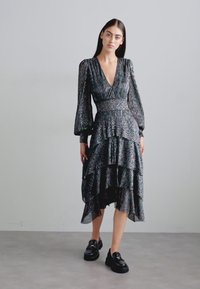 Robe noire avec des couches plissées, dotée de manches longues et d'un décolleté en V profond. Le tissu présente un motif texturé et chatoyant.