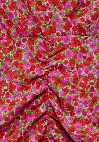 Tissu floral rouge et rose avec des feuilles vertes, présentant un détail froncé au centre.