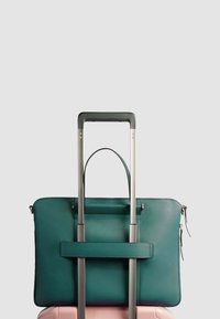 Een teal leren reistas ligt bovenop een roze koffer, met een handvat aan de bovenkant en een riem voor stabiliteit, voorzien van zilveren hardware en ritsen.