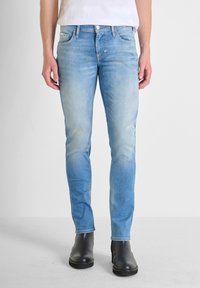 Jeans slim-fit de un azul claro, confeccionados en denim con un lavado desgastado, diseño de cinco bolsillos y acentos de costura, combinados con botines negros.