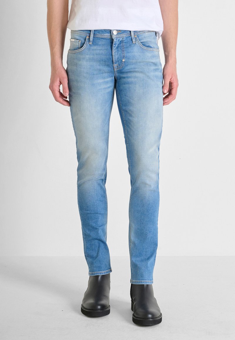 Jeans slim-fit de un azul claro, confeccionados en denim con un lavado desgastado, diseño de cinco bolsillos y acentos de costura, combinados con botines negros.