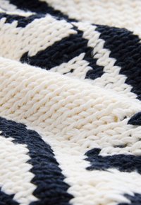 Textil tejido que presenta un esquema de colores crema y azul marino en un patrón geométrico, con un hilo grueso y texturizado de acabado suave.