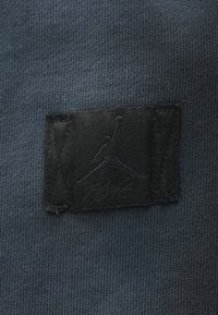 Μαύρο κεντημένο λογότυπο Jumpman σε επιφάνεια από σκούρο γκρι πλεκτό ύφασμα.