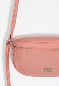 Miękka różowa torebka crossbody z regulowanym paskiem i srebrnym logo "BIMBA Y LOLA" z przodu, prezentowana na białym tle.