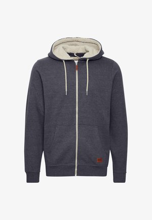 Mørkegrå hættetrøje med lynlås, cremefleecefór, forlommer og et læderlogo-patch nederst til venstre. Har snore til justering.