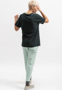 T-shirt in cotone nero con maniche corte, vestibilità rilassata e scollatura rotonda. Indossato con pantaloni tapered verde chiaro e sneaker con motivo.