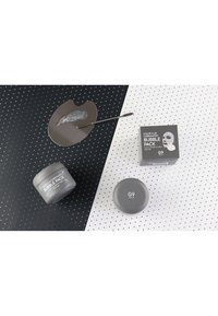 Un pot gris de pack de bulles, rond et avec une finition lisse, à côté d'une palette grise avec un échantillon d'argile et d'une boîte grise avec du texte blanc.