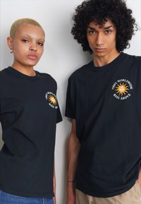 Sorte bomull t-skjorter med korte ermer, med et solgrafikk og tekst i oransje. Rett passform med rund hals.