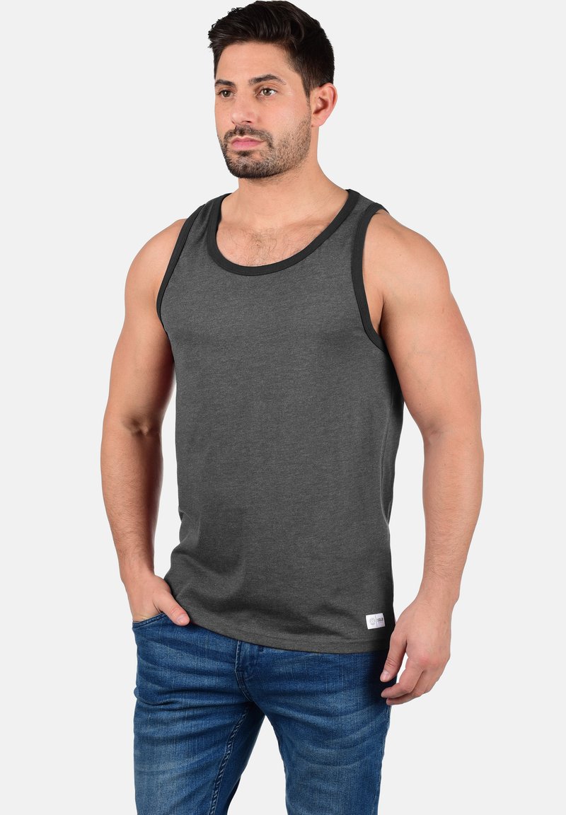 Graues Tanktop mit einem kontrastierenden schwarzen Halsausschnitt. Hergestellt aus weichem Stoff, mit lässigem Schnitt und Seitenähten. Getragen mit blauen Jeans.