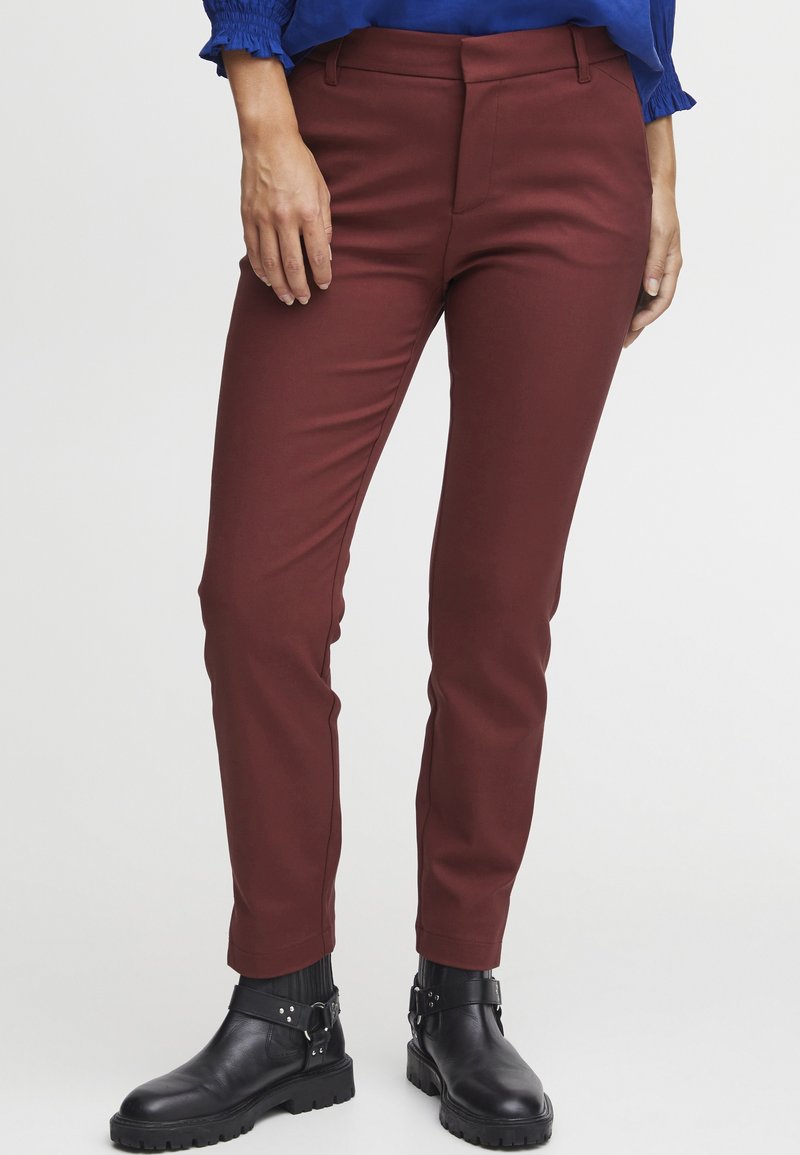 Burgundské slim-fit kalhoty vyrobené z hladké látky, s poloviční výškou pasu a bočními kapsami, doplněné černými kotníkovými botami.