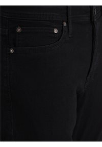 Mustat farkut, lähikuva sivusaumasta, jossa on kuparinväriset niitit taskuissa ja huomaamaton ompeluasiantuntija.