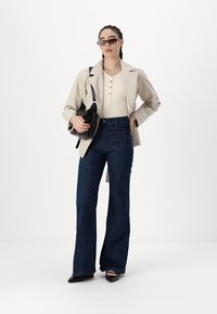 Blazer beige su un top a coste crema, abbinato a jeans a vita alta blu scuro a palazzo. Una borsa nera e delle ballerine appuntite completano il look.