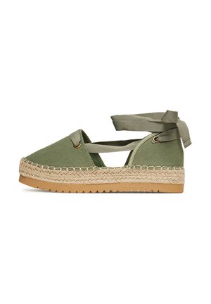 Alpargata de lona verde con suela de yute, con cordones cruzados en el tobillo y punta redondeada. Textura suave y detalles tejidos a lo largo de la suela.