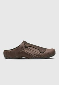 Calzado marrón tipo slip-on con un diseño liso y moldeado, y detalles texturizados. Presenta una suela de goma flexible y un sutil detalle de marca.