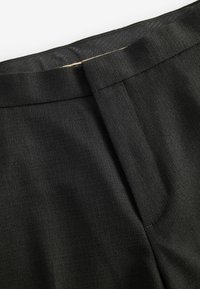 Tela negra texturizada, diseño ajustado, cinturilla visible y detalle de pliegue en la parte posterior. Forro interior suave en un color más claro.