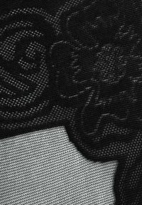 Zbliżenie na czarną koronkową tkaninę z kwiatowymi i geometrycznymi wzorami na białym tle.