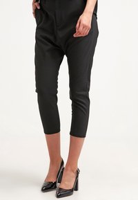 Černé zkrácené kalhoty vyrobené z hladké látky, s úzkým střihem a bočními kapsami, doplněné lesklými černými lodičkami na vysokém podpatku.