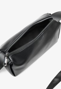Bolsa de cuero negro con forma rectangular, cierre de cremallera en la parte superior y una correa plana. Textura suave con hardware mínimo y sin patrones visibles.