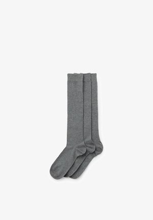 Trois paires de chaussettes grises unies montantes, soigneusement empilées avec les orteils orientés vers la gauche sur un fond blanc.