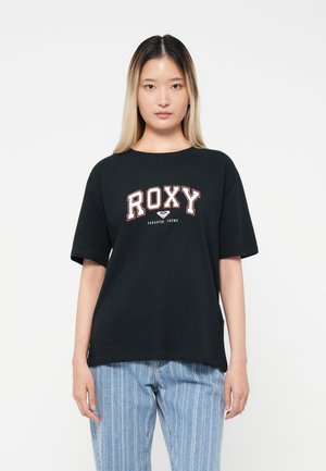 Black short-sleeve t-shirt with "ROXY" logo in white and red text, paired with light blue vertical-striped jeans. Smooth cotton fabric.