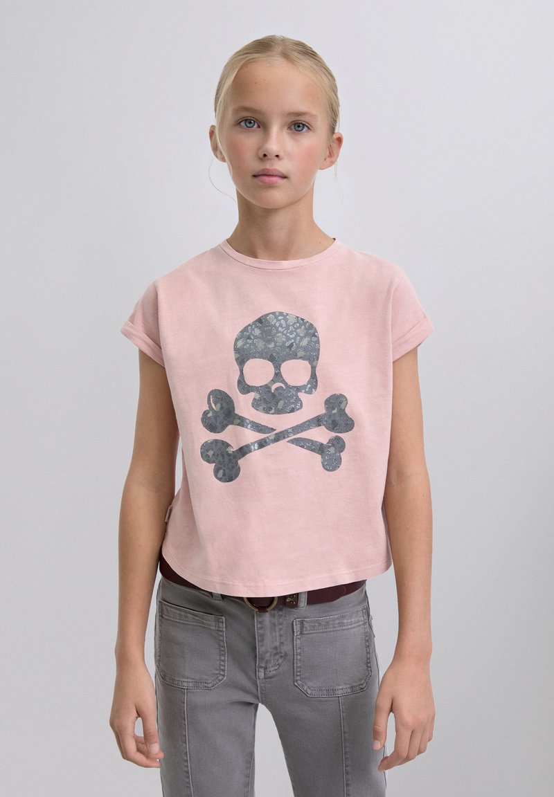 T-shirt rose à manches courtes avec un motif tête de mort et os croisés gris. Le tissu a une texture douce et un design court.