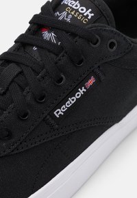 Svarta Reebok-sneakers med en ovandel av canvas, runda snörningar, vit gummisula och broderad logotyp med en Union Jack-accent.