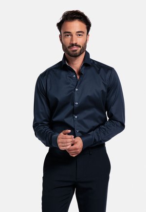 Marineblauw overhemd met een zachte textuur, lange mouwen en een knoopsluiting aan de voorkant met lichtgekleurde knopen. Getailleerde pasvorm.