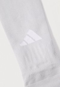 Κοντινή εικόνα ενός κάλτσας ανοιχτού γκρι υφασμάτινου με υφή, με διακριτικό λευκό μοτίβο τριών ρίγων λογότυπου κοντά στο πάνω μέρος.