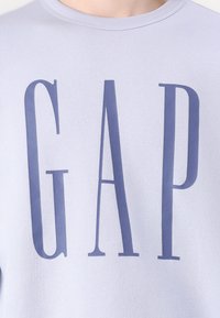 Ανοιχτό λεβάντα φούτερ με έντονα σκούρα μωβ γράμματα "GAP". Φτιαγμένο από μαλακό ύφασμα με στρογγυλή λαιμόκοψη και ριμπ μανσέτες.