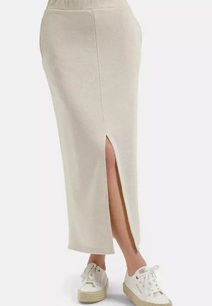 Beżowa spódnica midi z bocznym rozcięciem noszona z białymi sneakersami na platformie na białym tle.