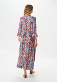 Robe maxi à motif floral avec des nuances de bleu, rouge et rose. Elle présente des manches à volants et un design fluide. Le tissu semble léger et texturé.