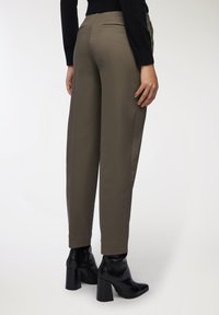 Pantaloni olive verdi a vita alta realizzati in tessuto liscio, con due tasche posteriori, abbinati a stivaletti neri con tacco.