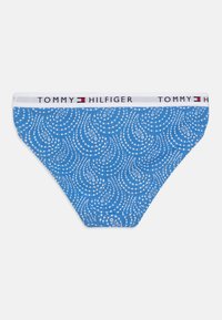 Kék mintás bikini alsó kanyarodó fehér pöttyökkel, fehér derékrésszel, amelyen "TOMMY HILFIGER" felirat látható fekete és piros részletekkel.