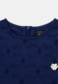 Marineblauwe jurk met een ronde halslijn, textuur met bloemenborduurwerk en een rits aan de achterkant. Voorzien van een zilveren hartvormige hardwareaccent.