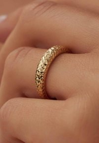 Goldring mit facettierter Textur, runder Form und glattem Inneren, der auf einer Hand mit natürlichem Hautton liegt.