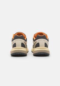 Sneaker grigie e crema con accenti arancioni, tomaia in rete, colli imbottiti e suola in gomma testurizzata con "SINCE 1936" impresso sul tallone.