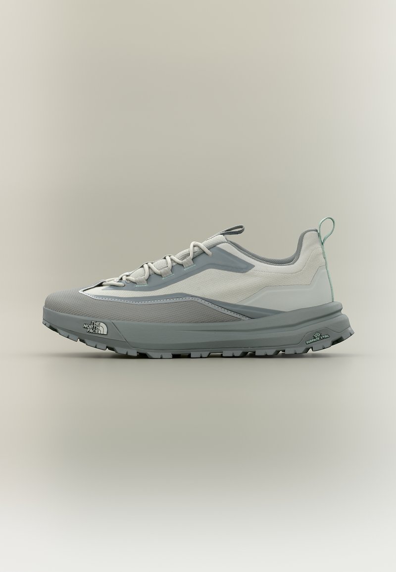 Ανοιχτό γκρι και λευκό παπούτσι πεζοπορίας με παχιά σόλα, λογότυπο στο πλάι, κορδόνια και ταινία έλξης στη φτέρνα, σχεδιασμένο για υπαίθριες δραστηριότητες.