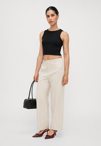 Top corto nero senza maniche, pantaloni beige a vita alta, borsa nera, scarpe con tacco borgogna, tessuto liscio, pantaloni dritti.