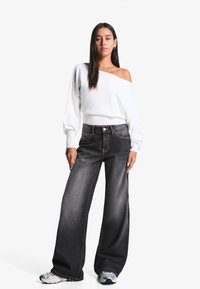 White off-the-shoulder sweater, ribbed hem; dark wide-leg jeans with contrast stitching; gray sneakers with silver accents.