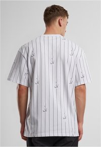 Bílá tričko s černými vertikálními pruhy a jemným listovým vzorem, s krátkými rukávy a volným střihem.