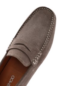 Mocasines de ante marrón con punta redondeada, costuras decorativas en blanco y un diseño de fácil puesta con una parte superior texturizada.