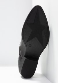 Semelle de chaussure noire présentant une surface texturée avec un motif étoilé. Le talon est d'un design noir uni avec un léger angle vers le haut.