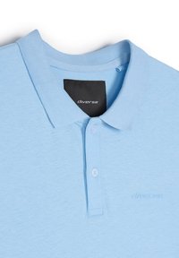 Jasnoniebieska koszulka polo z bawełny, z prążkowanym kołnierzykiem, trzema guzikami i wytłoczonym logo po lewej stronie.