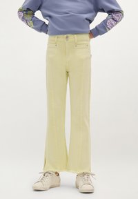Jeans flare giallo chiaro con orlo sfilacciato, dotati di vita aderente e due tasche frontali, abbinati a sneakers bianche.