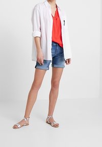 White button-up shirt, red v-neck top, blue denim shorts, and silver sandals. Casual outfit with light fabrics and relaxed fit.