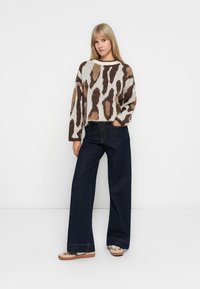 Brown and cream patterned knit sweater, wide dark denim pants, and light shoes. Sweater features a cropped design with long sleeves.