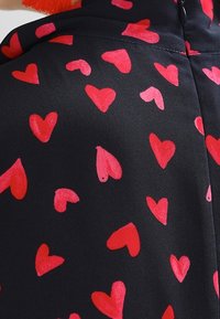 Zwarte stof met een patroon van harten in verschillende maten in rood en roze, met een gladde textuur en een subtiele glans.